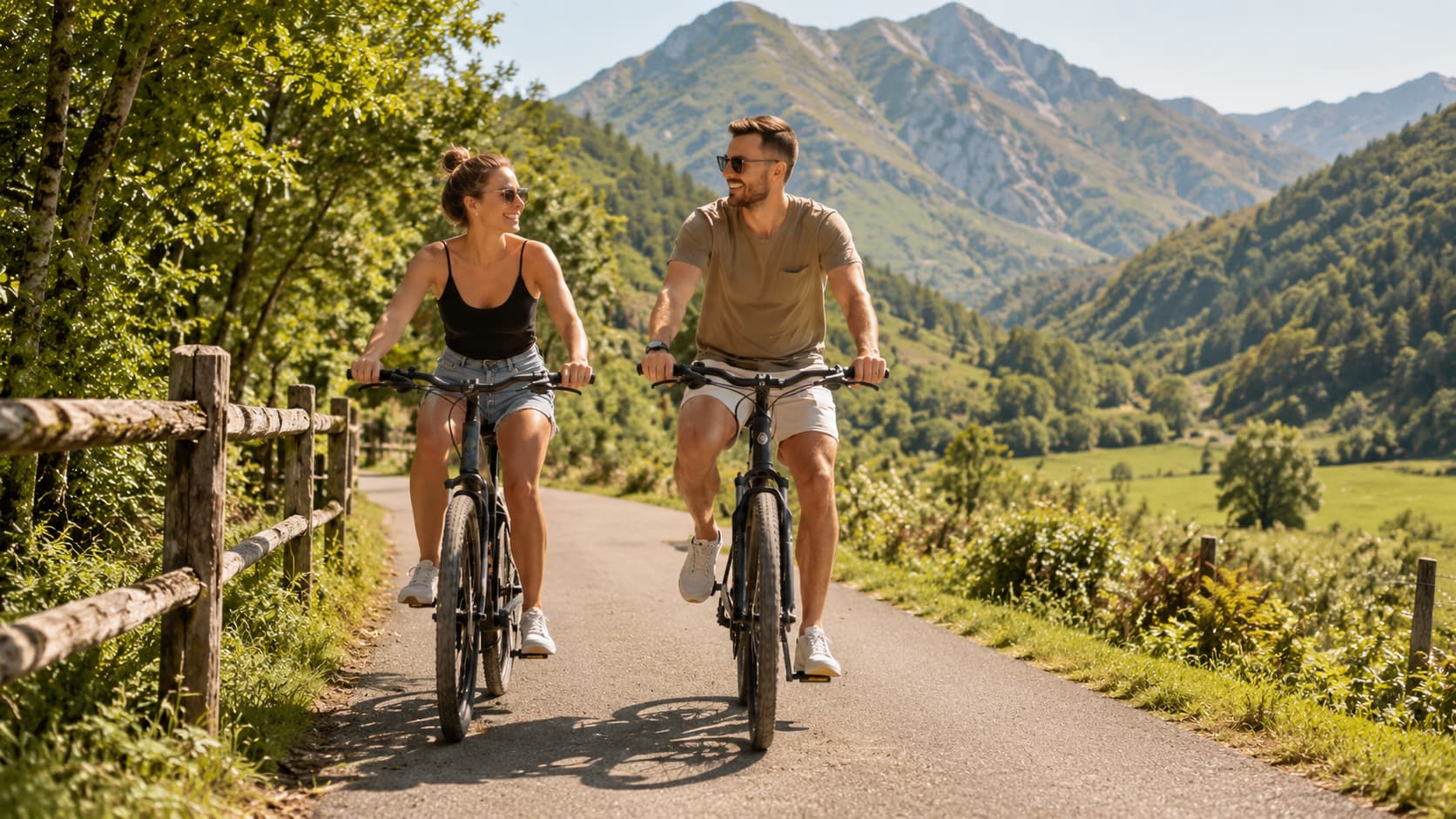 Pareja pedaleando por la Senda del Oso un día soleado de verano, con montañas verdes al fondo